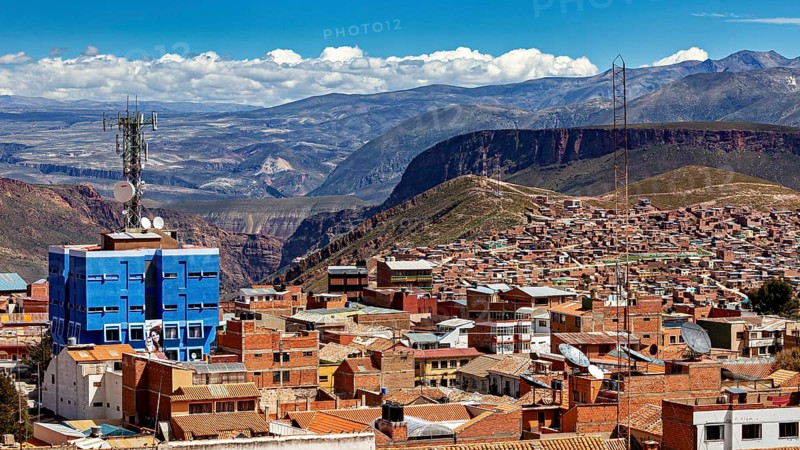 Urban landscape with red tiled roof architecture and a telecommunications tower in front of a cloudy mountain landscape, view over the city of Potosi in Bolivia