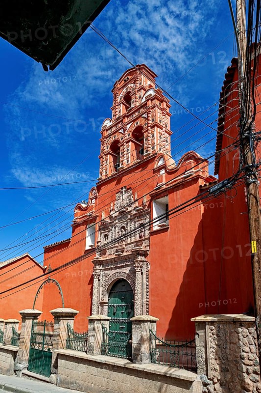 Colonial building with red façade and bell tower, surrounded by power lines and a clear sky, The churches of the city of Potosi in Bolivia