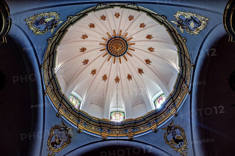 Dome of a church with golden decorations on a blue background and light through windows, inside the cathedral of Potosi in Bolivia
