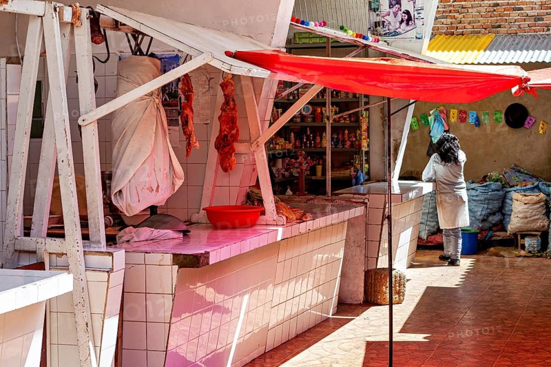 Market stall with meat on display, under a red sunshade, woman in the background, bright sunny day, The meat market in the market halls of Potosi in Bolivia