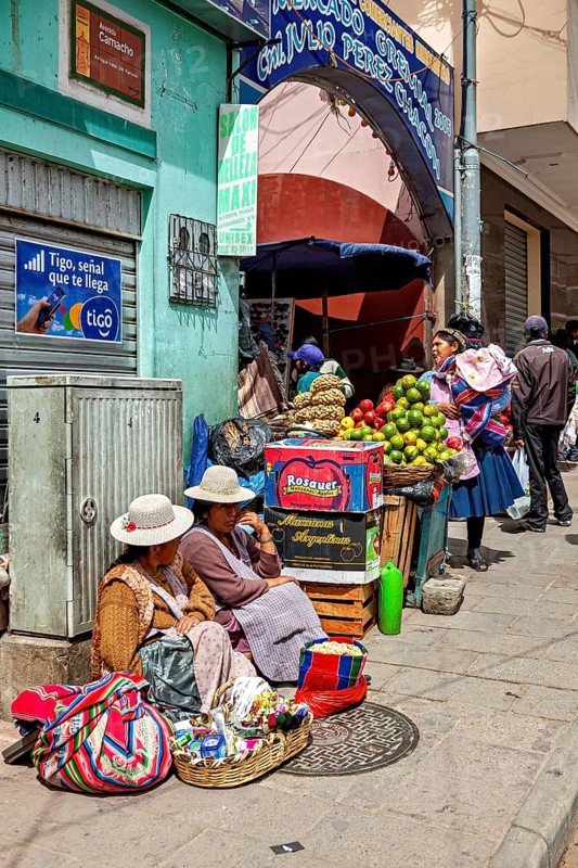 Women in traditional dress sell fruit at a busy market stall in a Bolivian town, selling goods in the market halls of Potosi in Bolivia