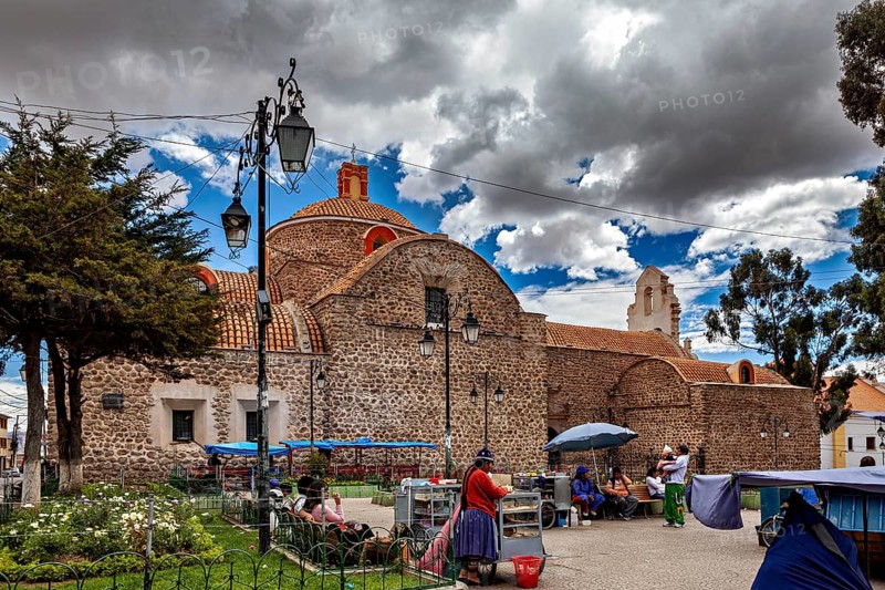 Small church with a round dome next to a busy market square under a partly cloudy blue sky, The old churches of Potosi in Bolivia
