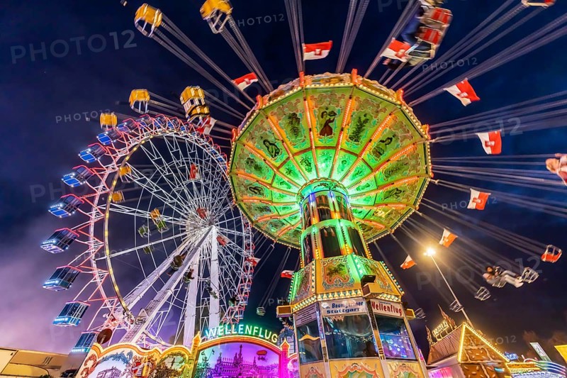 Folk festival time in Stuttgart. Ferris wheel and chain carousel in the evening. The 178th Cannstatter Volksfest on the Wasen is one of the most important traditional festivals in Germany. In addition to the large festival tents, the Wasen is characterised by fairground attractions. Around 320 showmen, festival hosts and market traders expect around four million visitors. Bad Cannstatt, Stuttgart, Baden-Württemberg, Germany