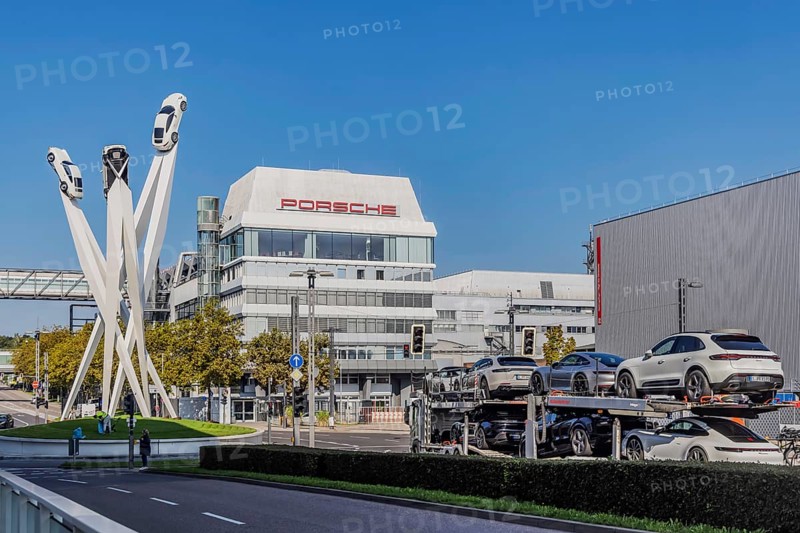 Porscheplatz with Porsche headquarters. Inspiration 911 artwork by Gerry Judah: three steles, each up to 24 metres high, presenting a Porsche 911. Car transporter with new cars. Stuttgart, Baden-Württemberg, Germany