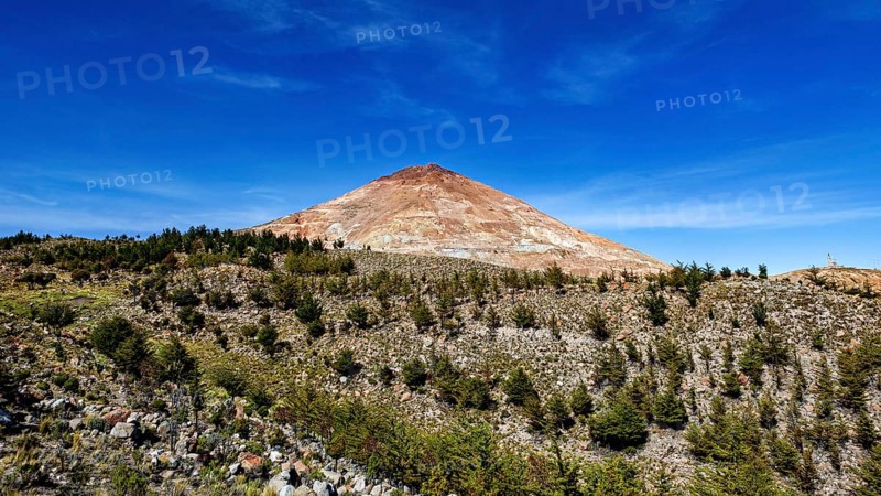 Brown volcanic mountain under a clear blue sky, surrounded by sparse vegetation and trees, the silver mountain Cerro Rico near Potosi Bolivia