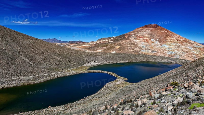 Volcanic mountain reflected in the lake, surrounded by barren landscape and under a bright blue sky, the silver mountain Cerro Rico near Potosi Bolivia