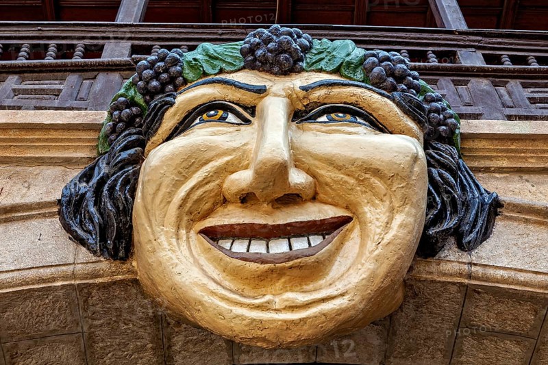 Stone mask with smiling face on an architectural structure, surrounded by green and brown tones, The face in the Museum of Potosi in Bolivia