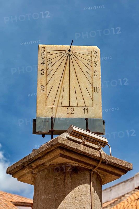 Stone sundial, mounted on a column, with dial and hands in front of a bright sky, The sundial of Potosi in Bolivia