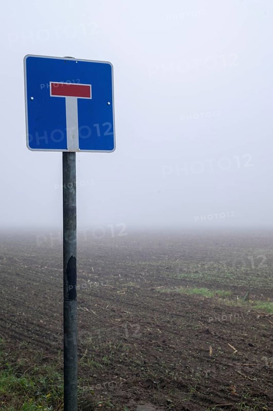 Dead end sign standing on a pole in a tilled field with thick fog