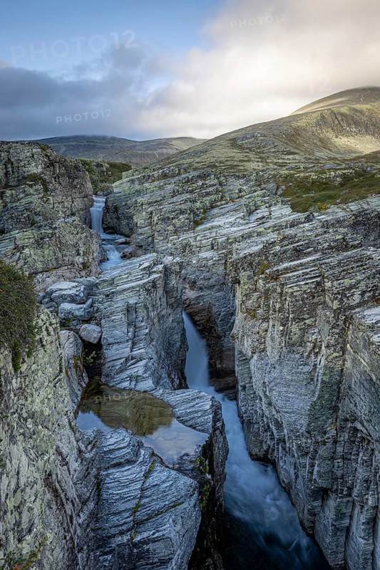 Deep gorge with a clear watercourse, surrounded by majestic rocks and mountains with a waterfall running through it, Peer Gynt hytta, Rondane National Park, Otta, Innlandet, Norway