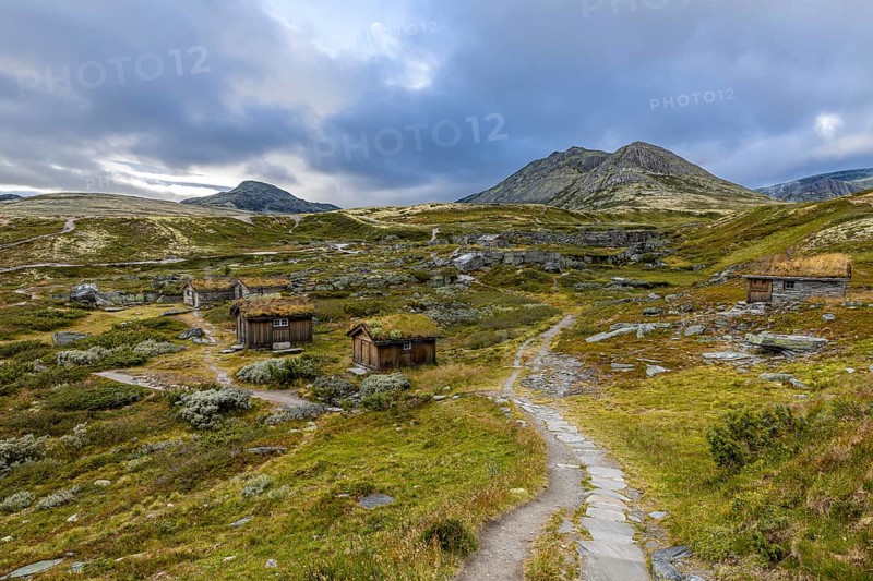 Wooden huts in an open meadow in a remote mountain landscape, with winding paths and clouds in the sky, Peer Gynt hytta, Rondane National Park, Otta, Innlandet, Norway