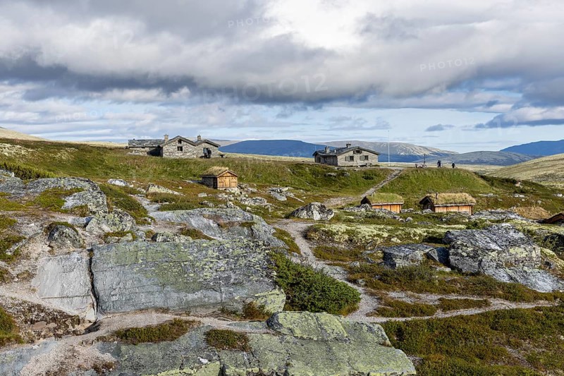 Various wooden cabins on a rocky plain, surrounded by grass and mountains under a cloudy atmosphere, Peer Gynt hytta, Rondane National Park, Otta, Innlandet, Norway