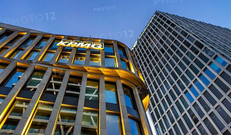 The picture shows modern office and commercial buildings at the central station, KPMG and Total Energie logo on the facade, warm evening light, frog perspective, Berlin, Germany