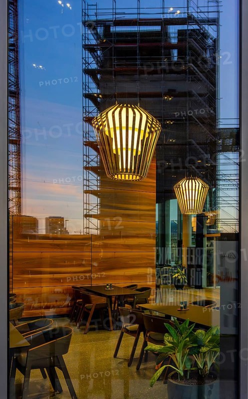 The picture shows the interior of a modern Berlin pub, taken in the evening. The scene is characterised by modern lighting fixtures reminiscent of large, glowing light bulbs. Scaffolding can be seen through the glass window, Berlin, Germany