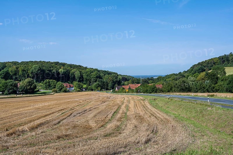 View of a harvested field with neighbouring village and wooded hills under a clear sky, Halle, Westphalia
