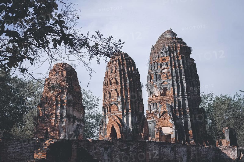 Tall brick ruins and towers reaching towards the sky amidst surrounding trees, evoking antiquity. Wat Chaiwatthanaram in Ayutthaya, Thailand