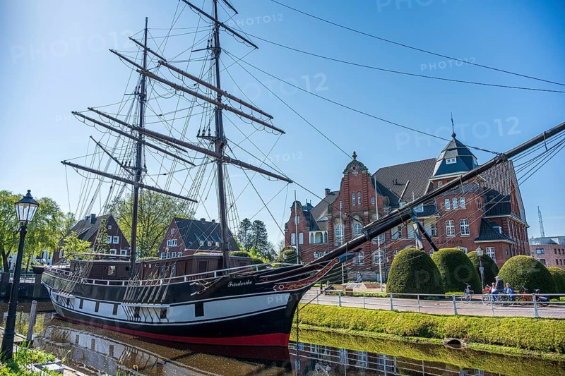 A historic sailing ship on a sunny day with a striking brick building in the background, The sailing ship Frederike von Papenburg in front of the town hall in Papenburg
