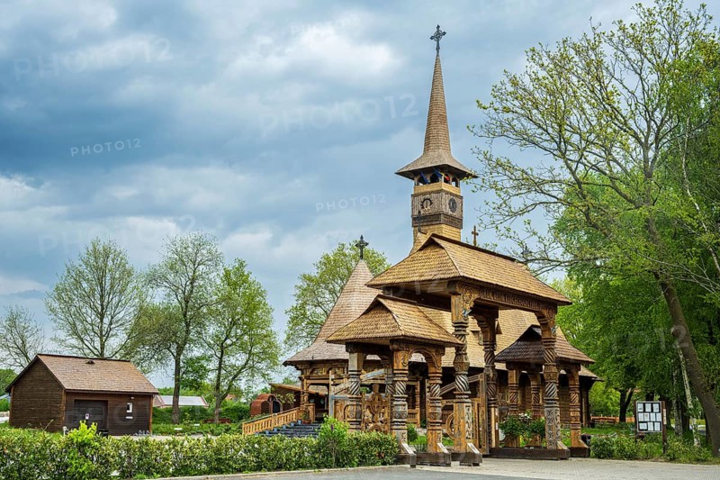 Impressive wooden church with elaborate wood carvings, surrounded by trees under a cloudy sky, The Romanian Orthodox church near Sögel in Emsland