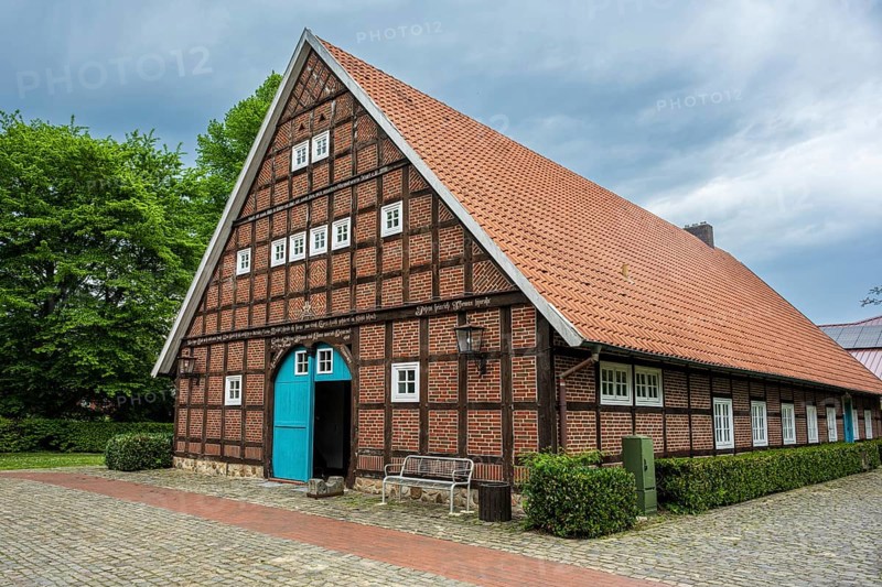 Traditional half-timbered house with red tiled roof and green surroundings under a cloudy sky, farmhouse in Sögel Emsland