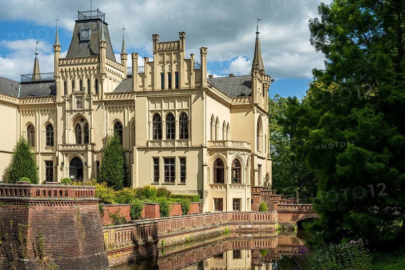 Gothic castle with moat and battlements, flanked by lush trees, Evenburg Castle, Leer, East Frisia
