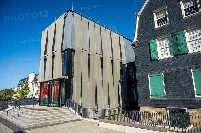 Modern building with a striking façade and large glass windows next to a traditional house under a blue sky, Museum of Early Industrialisation in Wuppertal Barmen