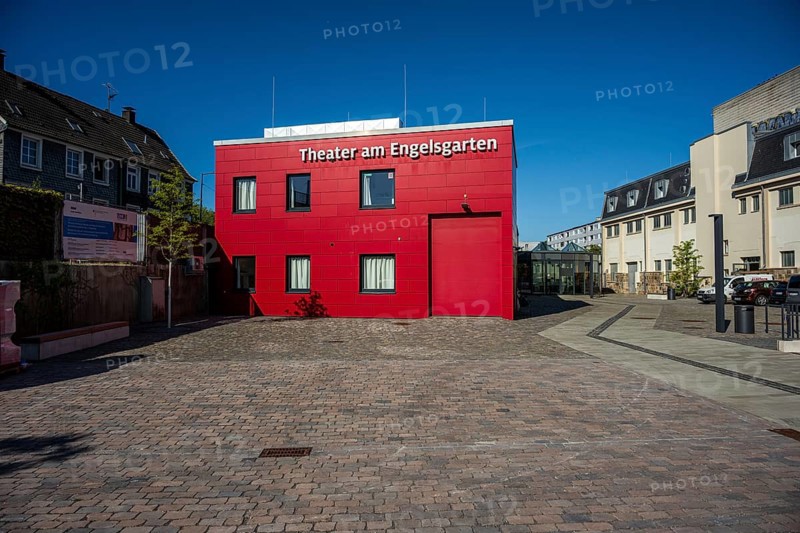 Theatre building in red with cobblestones surrounded by urban elements, high-contrast design, Theater am Engelsgarten in Wuppertal Barmen
