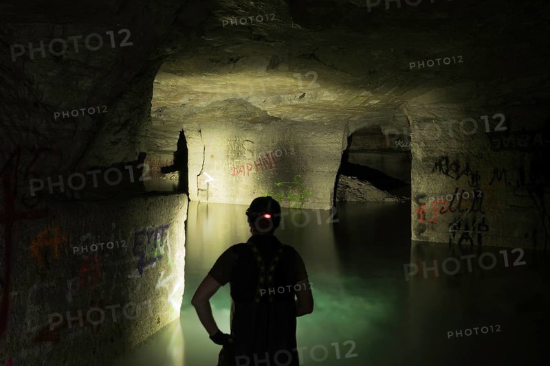 Person exploring illuminated, water-filled mine with graffiti, Ofenkaulen, Lost Place, Königswinter, North Rhine-Westphalia, Germany