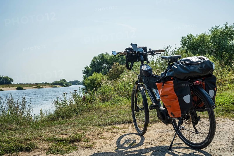 A bike with panniers stands on a sunny riverbank, embedded in nature, Weser cycle path, Weser, touring bike