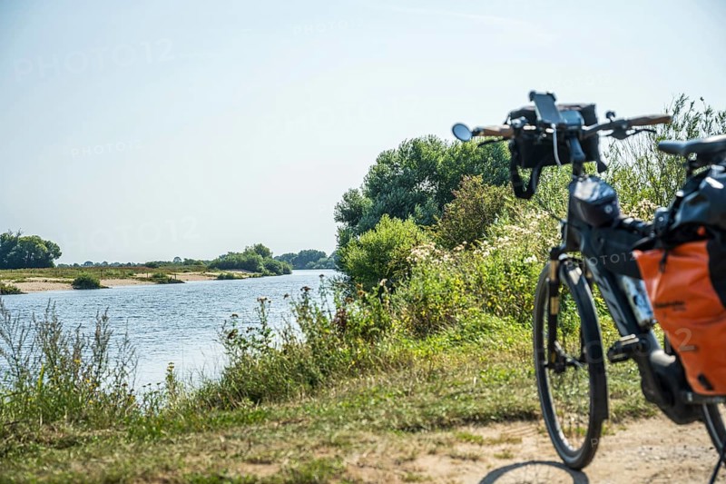A bicycle stands on the riverbank, surrounded by a green landscape under a clear sky, Weser cycle path, Weser, touring bike