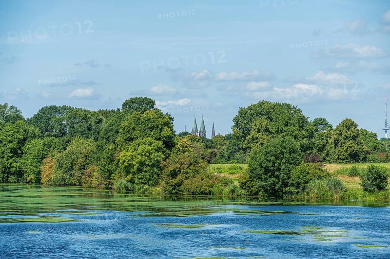 A river with green foliage, church towers in the background and blue sky, Weser cycle path, Weser, Werdersee, Neustadt, Bremen, Bremen, Germany