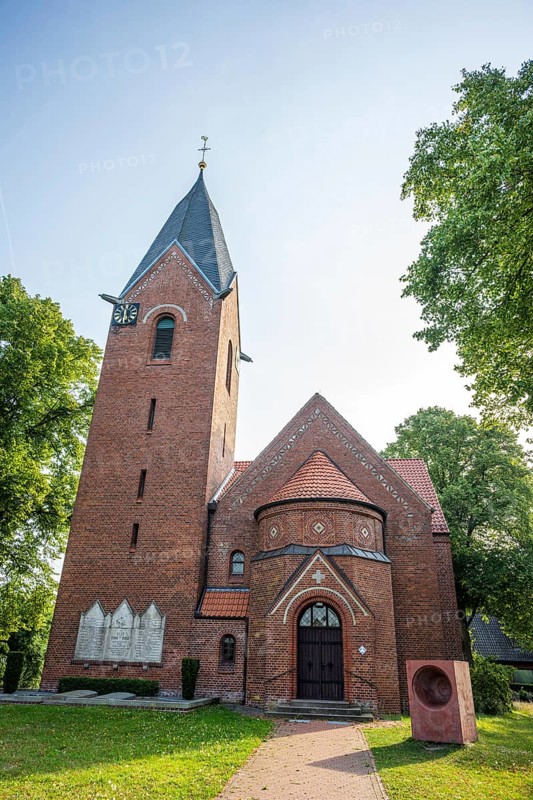 Brick church with Gothic tower and clock, surrounded by green trees under a blue sky, Weser cycle path, Kreuzkirche Schweringen, Schweringen Nienburg Weser, Lower Saxony