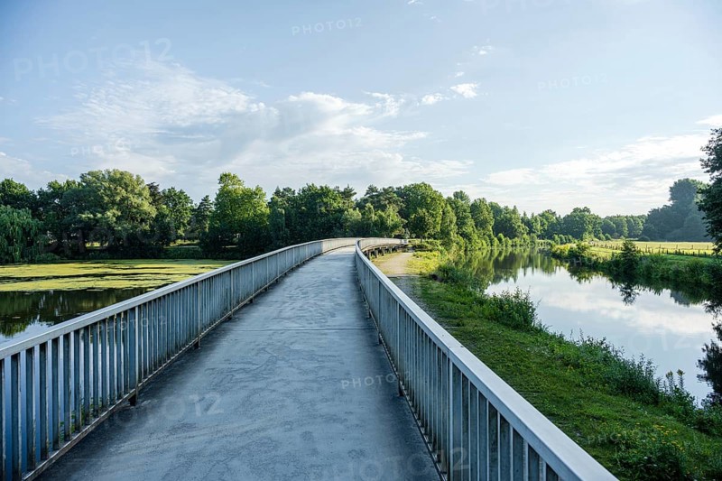 Bridge along a quiet river, green surroundings and blue sky reflected in the water, Emssee near Warendorf, Münsterland