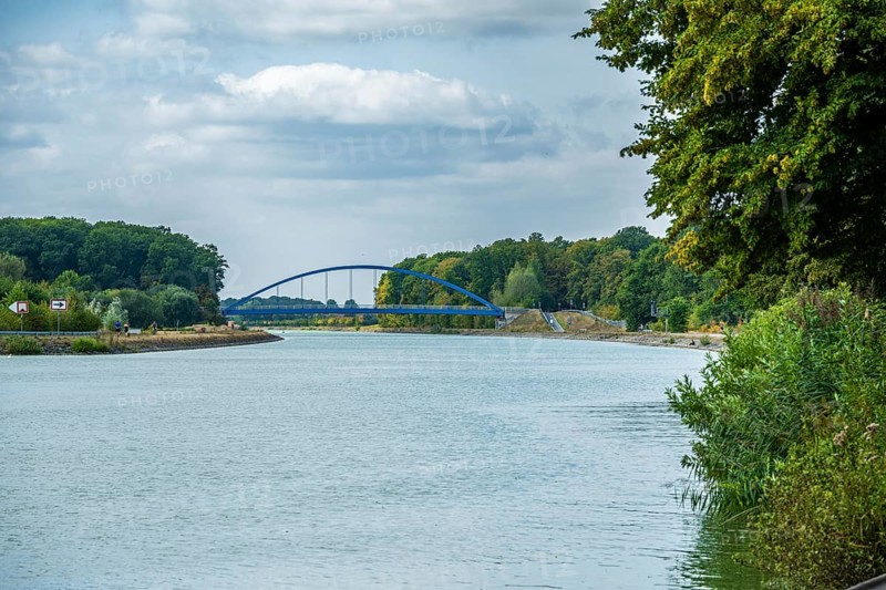 View of a canal with a modern blue bridge under a cloudy sky, surrounded by green trees, Senden, Münsterland, North Rhine-Westphalia, Germany