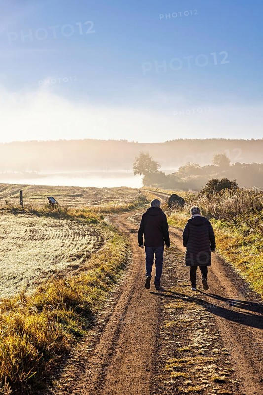 Two people walking on gravel road in the countryside a misty autumn morning, Sweden