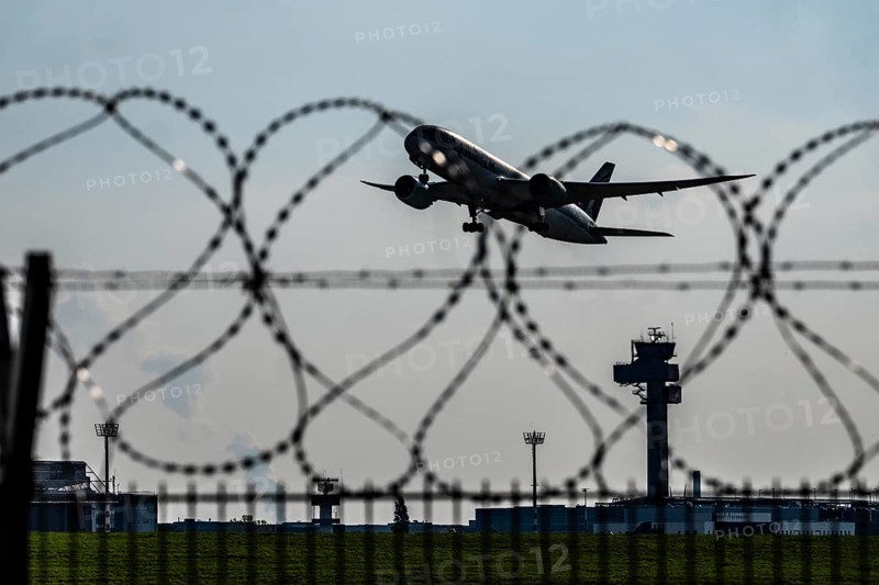 Symbolic image security at the airport, outer fence at Düsseldorf International Airport, steel wire fence, with S-wire rolls, NATO wire, on the top of the fence, aircraft taking off, air traffic control tower, DFS, North Rhine-Westphalia, Germany