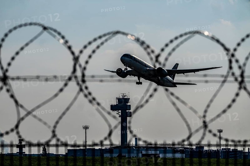 Symbolic image security at the airport, outer fence at Düsseldorf International Airport, steel wire fence, with S-wire rolls, NATO wire, on the top of the fence, aircraft taking off, air traffic control tower, DFS, North Rhine-Westphalia, Germany