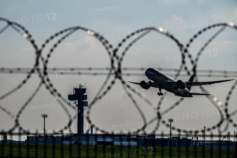 Symbolic image security at the airport, outer fence at Düsseldorf International Airport, steel wire fence, with S-wire rolls, NATO wire, on the top of the fence, aircraft taking off, air traffic control tower, DFS, North Rhine-Westphalia, Germany