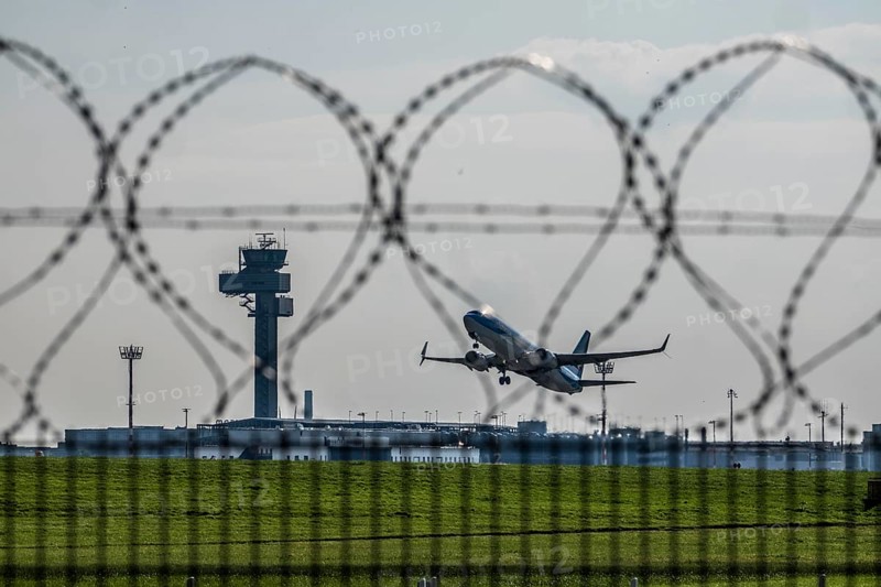 Symbolic image security at the airport, outer fence at Düsseldorf International Airport, steel wire fence, with S-wire rolls, NATO wire, on the top of the fence, aircraft taking off, air traffic control tower, DFS, North Rhine-Westphalia, Germany