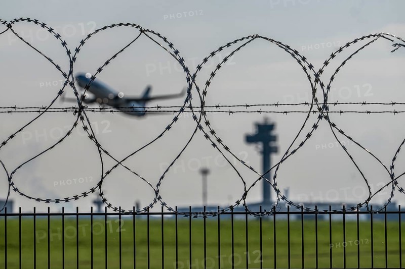 Symbolic image security at the airport, outer fence at Düsseldorf International Airport, steel wire fence, with S-wire rolls, NATO wire, on the top of the fence, aircraft taking off, air traffic control tower, DFS, North Rhine-Westphalia, Germany