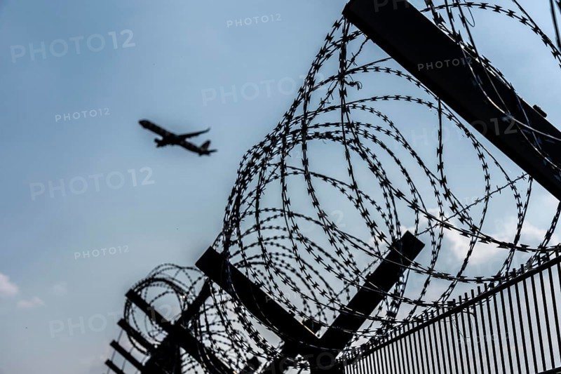 Symbolic image security at the airport, outer fence at Düsseldorf International Airport, steel wire fence, with S-wire rolls, NATO wire, on the top of the fence, aeroplane taking off, North Rhine-Westphalia, Germany