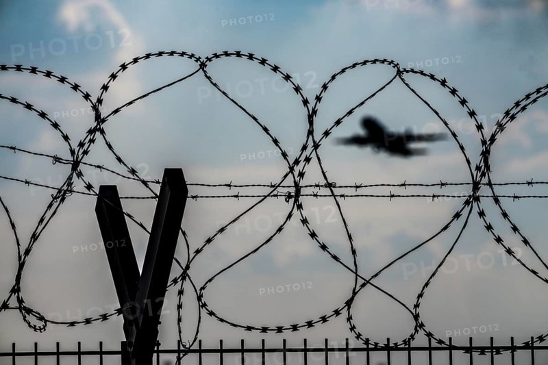 Symbolic image security at the airport, outer fence at Düsseldorf International Airport, steel wire fence, with S-wire rolls, NATO wire, on the top of the fence, aeroplane taking off, North Rhine-Westphalia, Germany