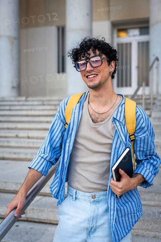 Young man with a backpack and a notebook, smiling while walking up the modern building stairs, representing education, collegiate life, and future opportunities