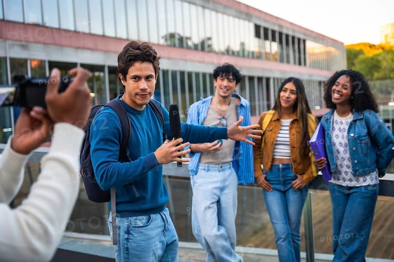 Young diverse students collaborating on a media project, a man holding a boom microphone interviewing peers while another person films on a university campus