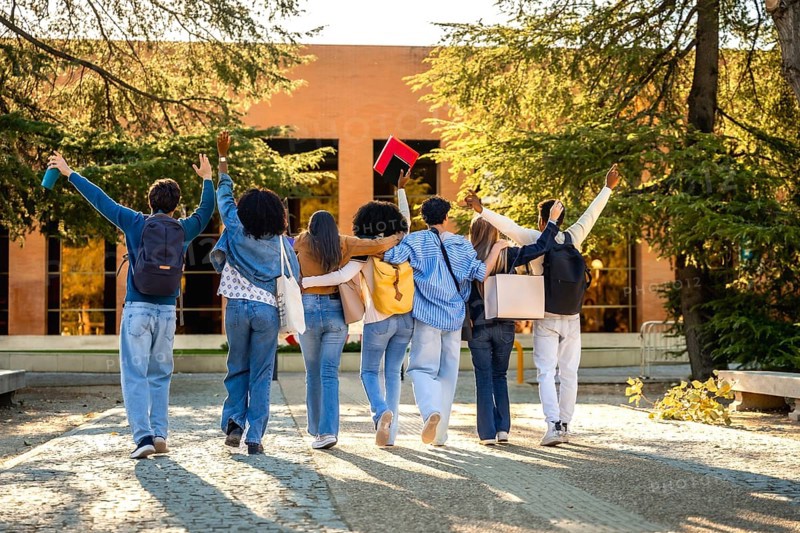 Group of diverse university students walking together on campus, embracing friendship and education, raising arms in success and celebration of their college journey