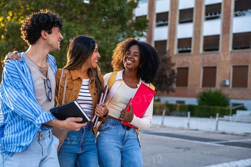 Group of diverse university students walking together on campus, smiling, holding notebooks and binders, representing friendship, education, and multicultural learning