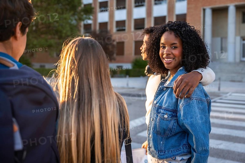 Diverse group of young students smiling and walking on a university campus during sunset, representing friendship, education, and youth while heading to class or spending time together