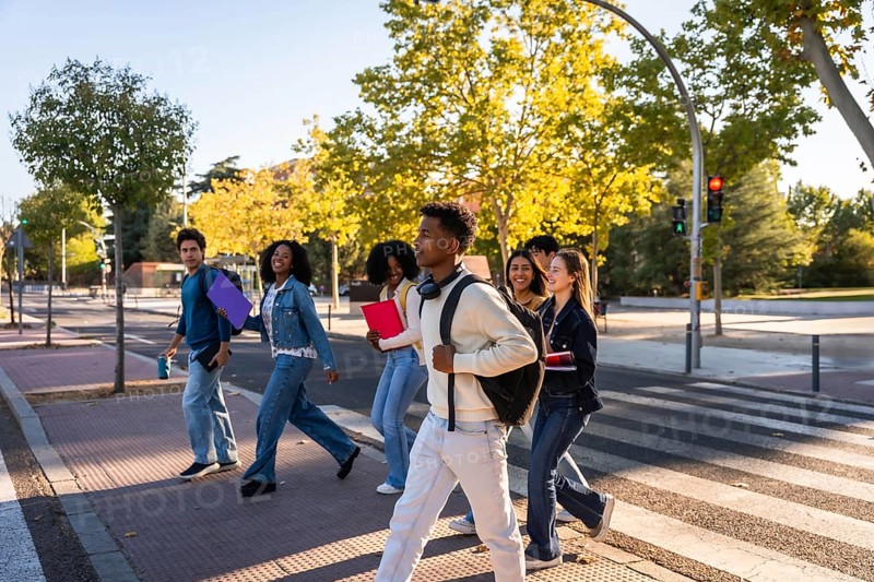 Multi ethnic group of university students walking across a campus crosswalk, smiling and chatting as they carry backpacks and books, symbolizing friendship, learning and youthful energy