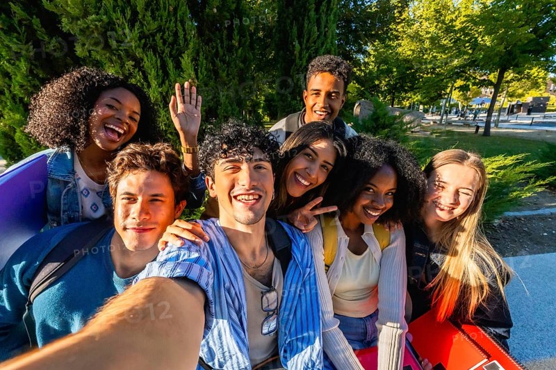 Group of happy multicultural young adult friends smiling and posing for a selfie while standing outdoors on a vibrant university campus, celebrating unity and friendship