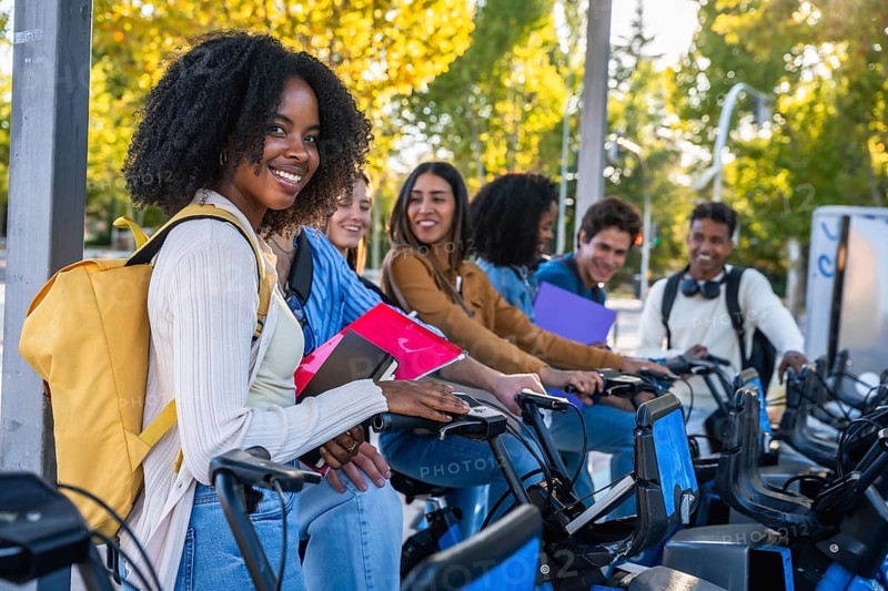 Group of happy multiracial university students smiling and preparing to use shared bicycles from a city station, promoting sustainable urban mobility and friendship