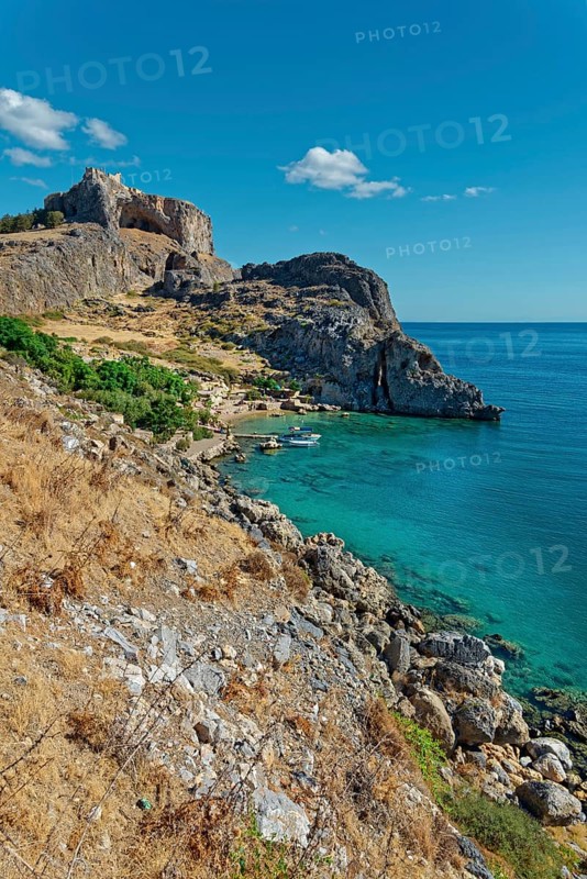Steep cliffs Paulus Bay of Lindos over crystal clear blue water under a bright blue sky, Acropolis, Lindos, Rhodes, Island, Greece
